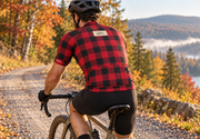 Rider seen from behind on a gravel road in fall, wearing The Lumberjack jersey with the CORBAH TIMBER CO. back label. Bib shorts sold separately.