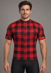 Rider wearing The Lumberjack cycling jersey: red and black buffalo check with printed button placket, chest pockets and collar points. Bib shorts sold separately.