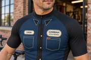 Close-up of The Mechanic jersey chest: printed collar points, charcoal placket with cream buttons beside the zip, CREW name patch, CORBAH CYCLE WORKS badge and chest pockets with a rust tab.