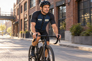 Cyclist in The Mechanic navy and charcoal work-shirt jersey riding past brick warehouses in morning sun. Bib shorts sold separately.