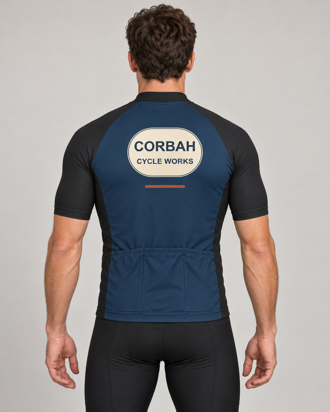 Back of The Mechanic jersey on a rider: navy body, charcoal raglan sleeves, CORBAH CYCLE WORKS badge with rust dash and three plain navy rear pockets. Bib shorts sold separately.