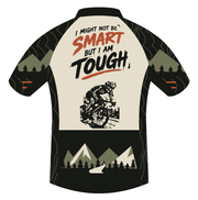 Back artwork of the Corbah TOUGH jersey: hand-lettered slogan I MIGHT NOT BE SMART BUT I AM TOUGH with SMART in rust, a gritty stencil-style rider below, and an olive and bone mountain scene with a winding road across the black rear pockets.